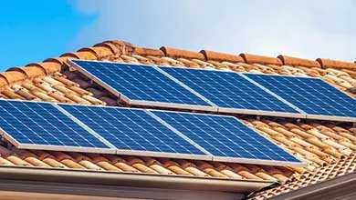 Solar panels on a reddish-brown tile roof under a clear blue sky.