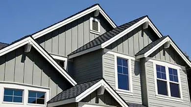Modern house gables: gray siding, white trim, dark shingled roof, clear blue sky.