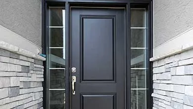 Black paneled front door with silver hardware, centered between two tall sidelight windows in a gray stacked stone wall.