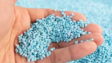 A close-up of a hand cupping small, light blue plastic granules.