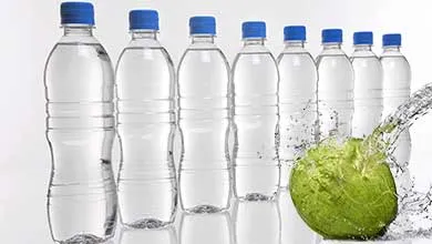A green coconut being splashed with water in front of several plastic water bottles with blue caps.